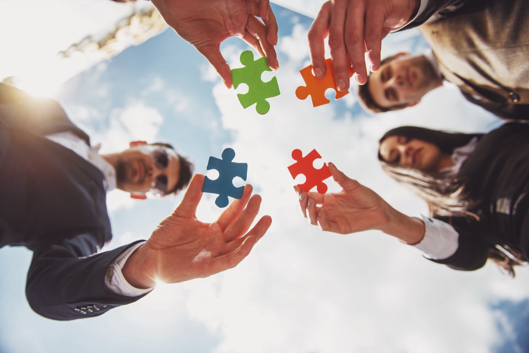 Four marketers are standing outside, putting four different puzzle pieces together to build a complete marketing strategy.