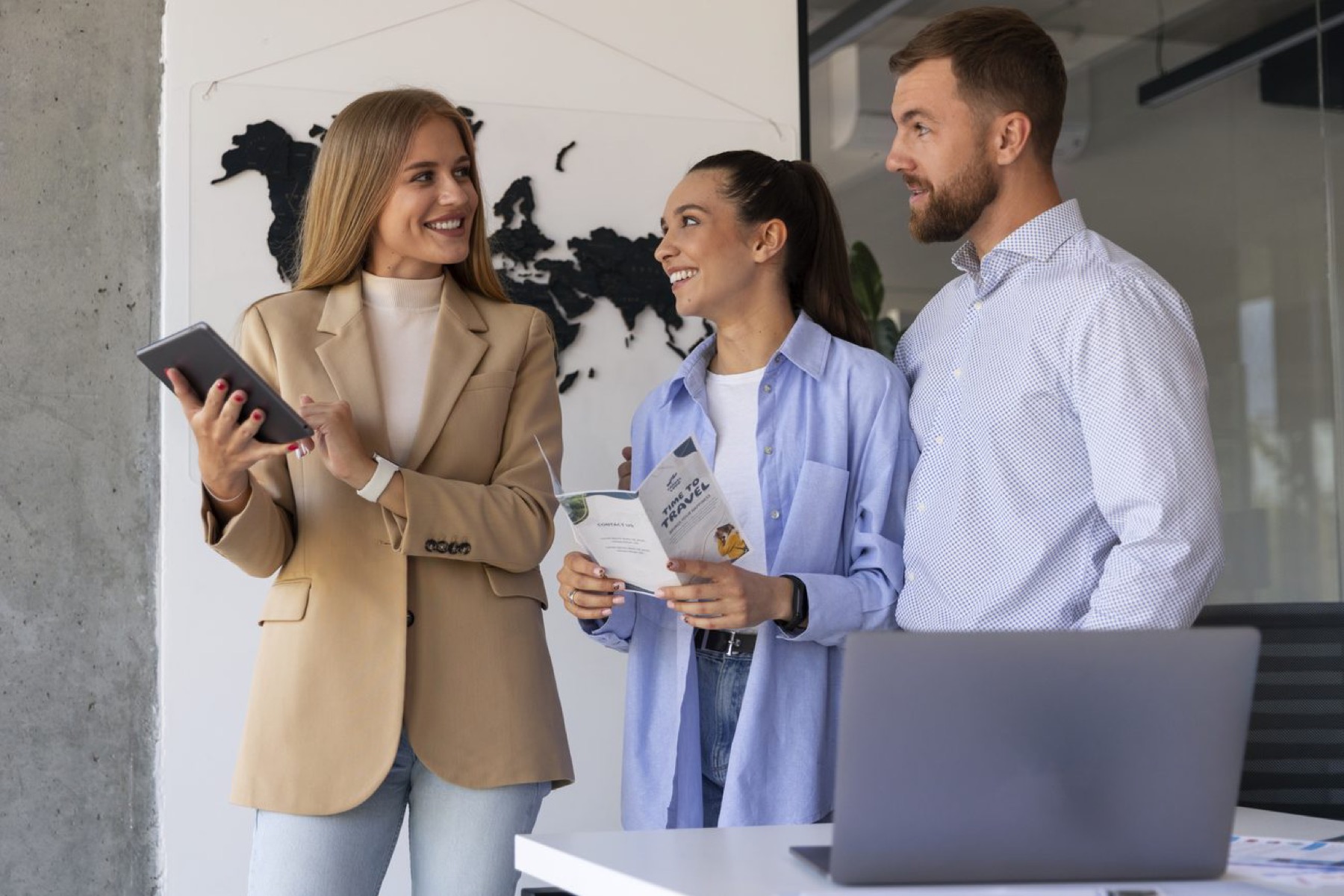 Three marketers are standing in the hallway of a bright office, happily in conversation with smiles on their faces.