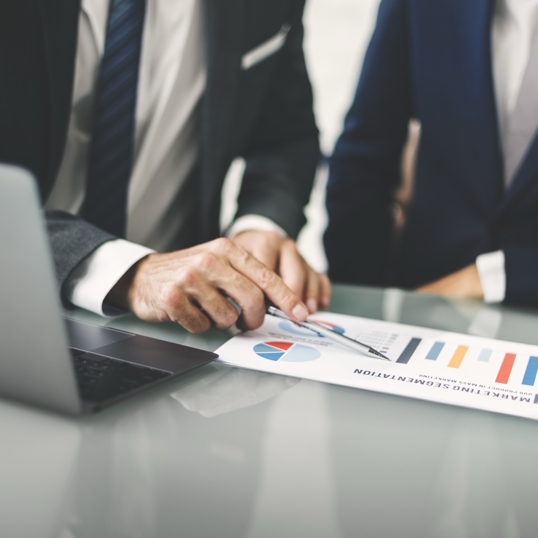 A team looks over a marketing segmentation chart, examining the audience analytics of their clients. They are all dressed in suits and sitting in front of an open laptop.